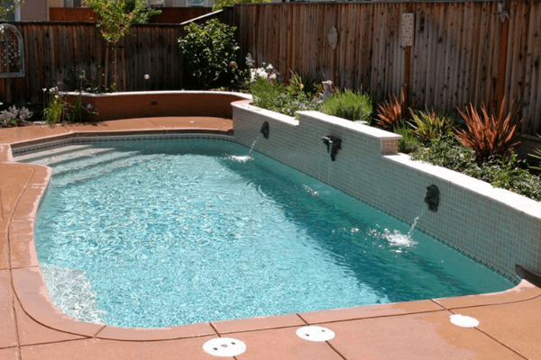 Backyard swimming pool with turquoise water, tan deck, and a curved built-in spa beside a wooden fence