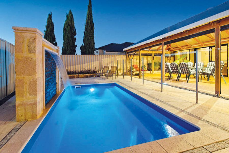 Backyard pool with a waterfall, covered patio, and blue evening sky