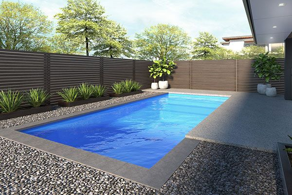 Modern backyard with a rectangular blue pool, gray deck, and surrounding green plants and fence
