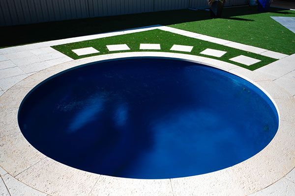 Blue circular pool or fountain embedded in a light stone patio with green geometric tiles nearby