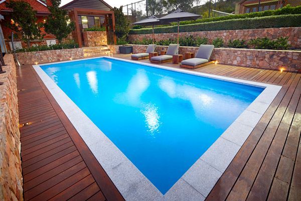 Outdoor backyard pool with blue water, wooden deck, lounge chairs, and garden seating area