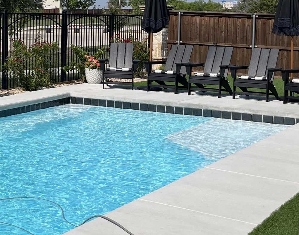 Backyard pool with blue water, patio chairs, and a fence in the background