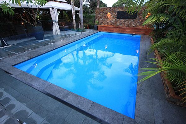 Backyard swimming pool with bright blue water, surrounded by stone paving and tropical plants