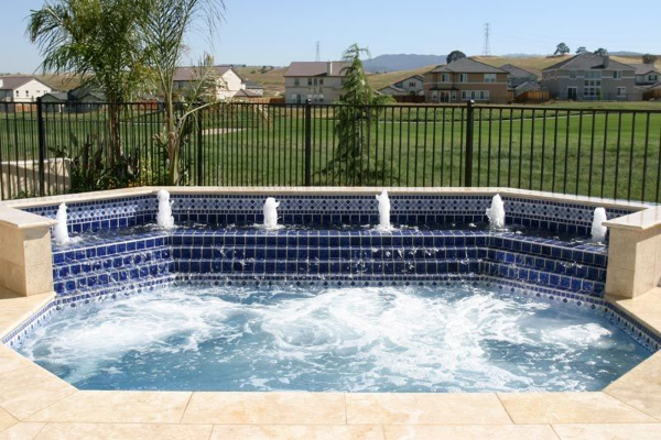 Outdoor backyard spa with blue tile, bubbling water, and a black metal fence in the background