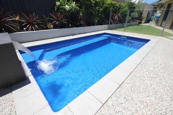 Rectangular blue swimming pool with water jets in a landscaped backyard