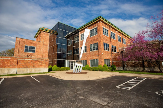 Modern brick building with glass entrance, under blue sky, beside a parking lot and blooming tree