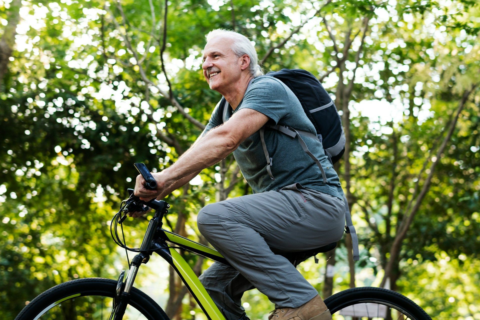 Cyclist riding a bike on a leafy trail with a backpack, smiling in daylight