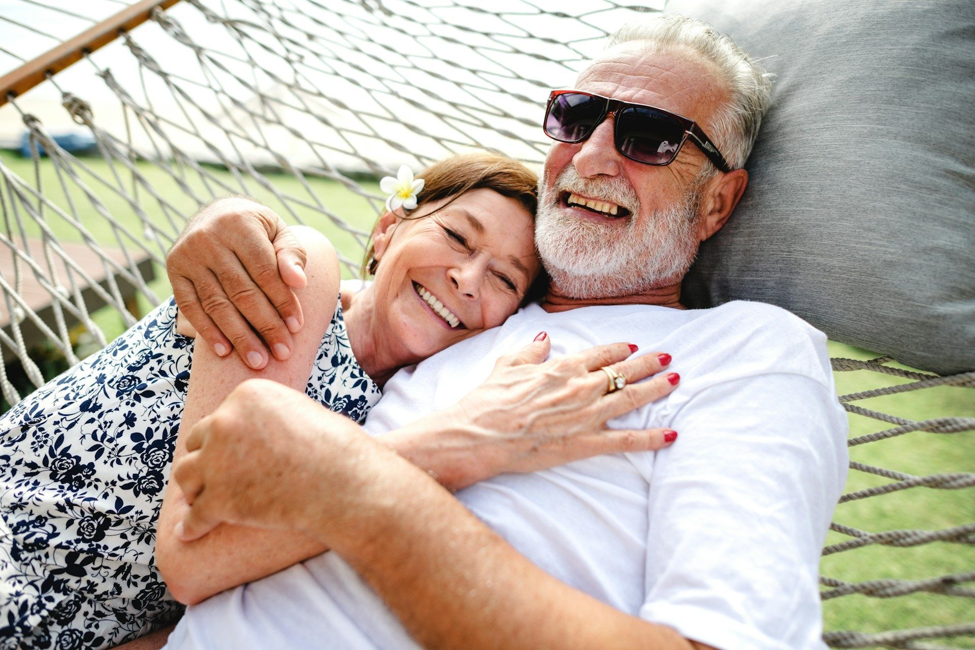 Smiling couple hugging in a hammock outdoors, with the man wearing sunglasses