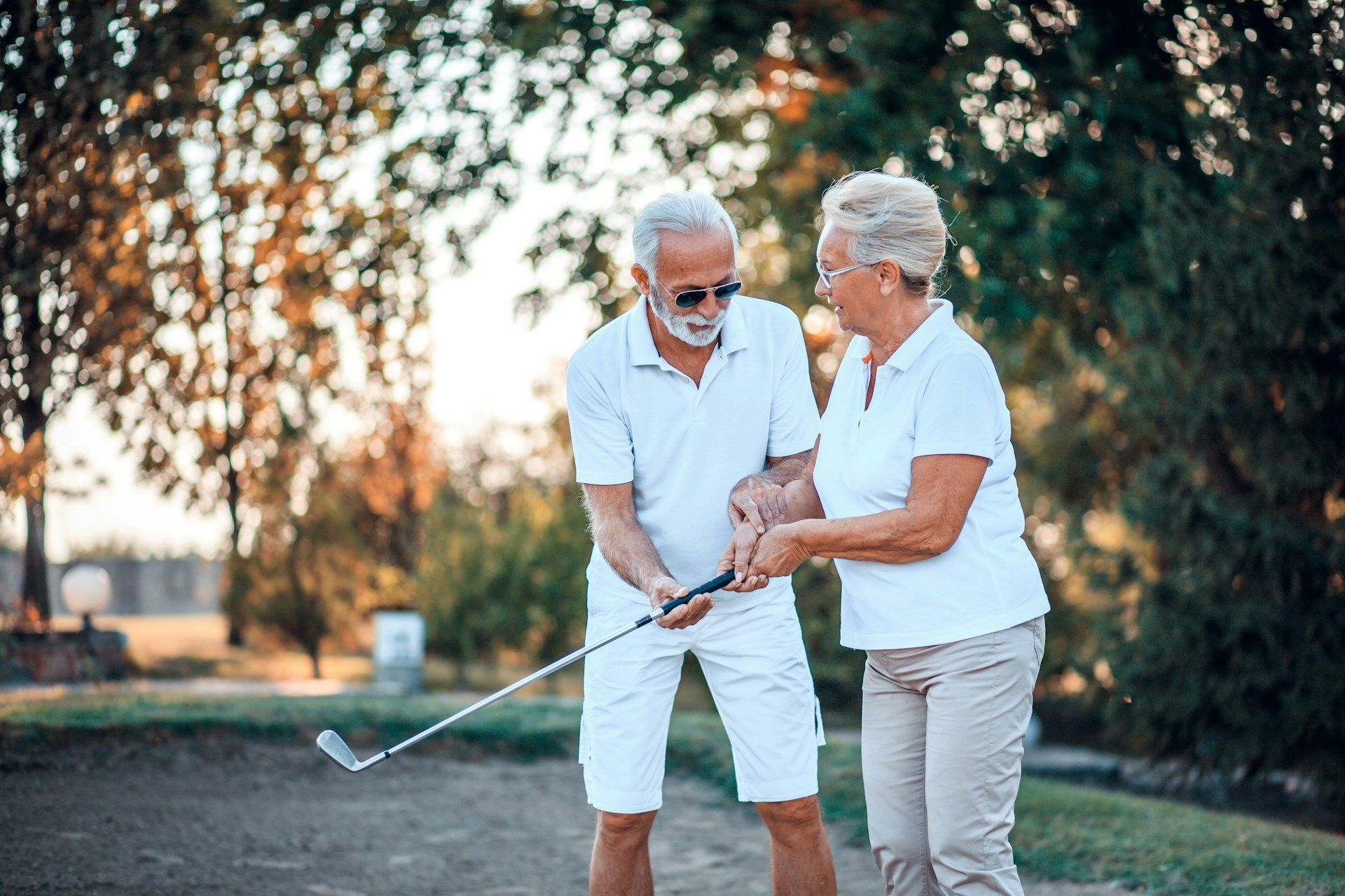 Two people chatting on a golf course, holding a club and smiling in warm sunlight
