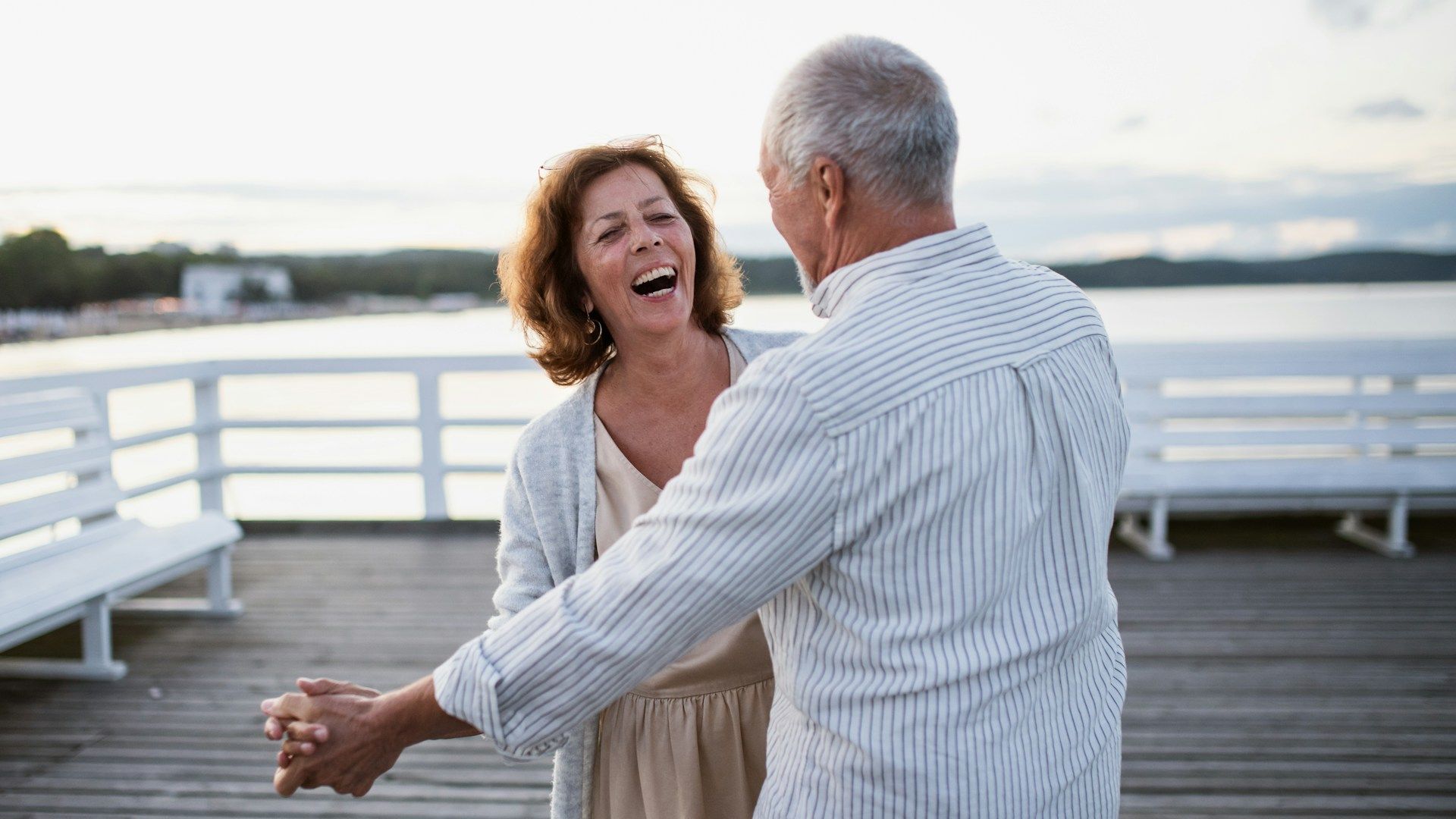 Couple laughing and dancing on a wooden pier by the water at sunset