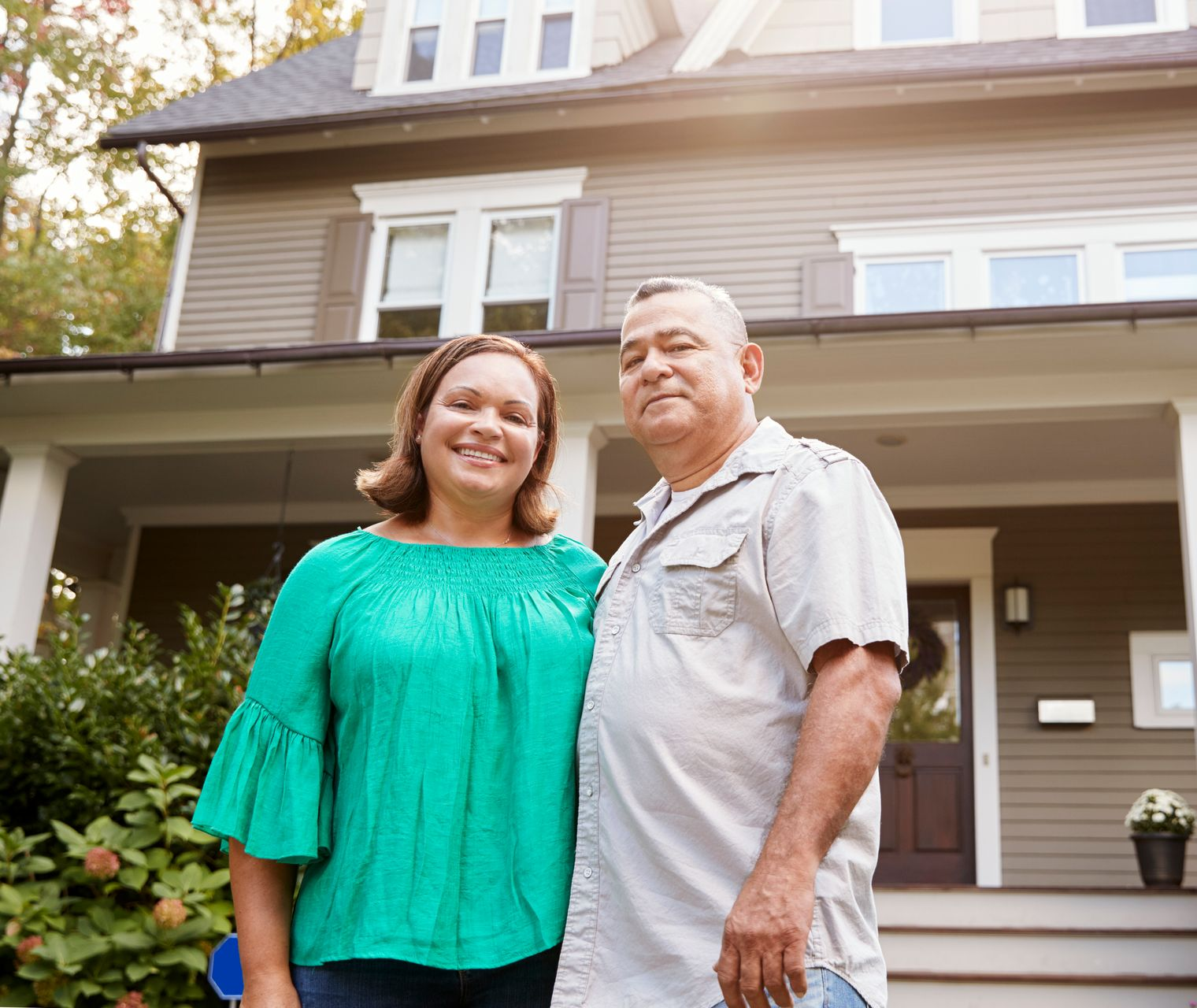 Two people standing in front of a house, smiling at the camera.