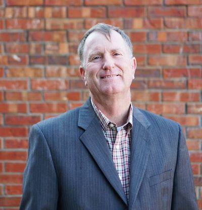 Smiling man in a gray blazer standing before a brick wall