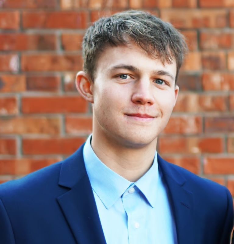 Portrait of a person in a blue blazer and light blue shirt against a brick wall