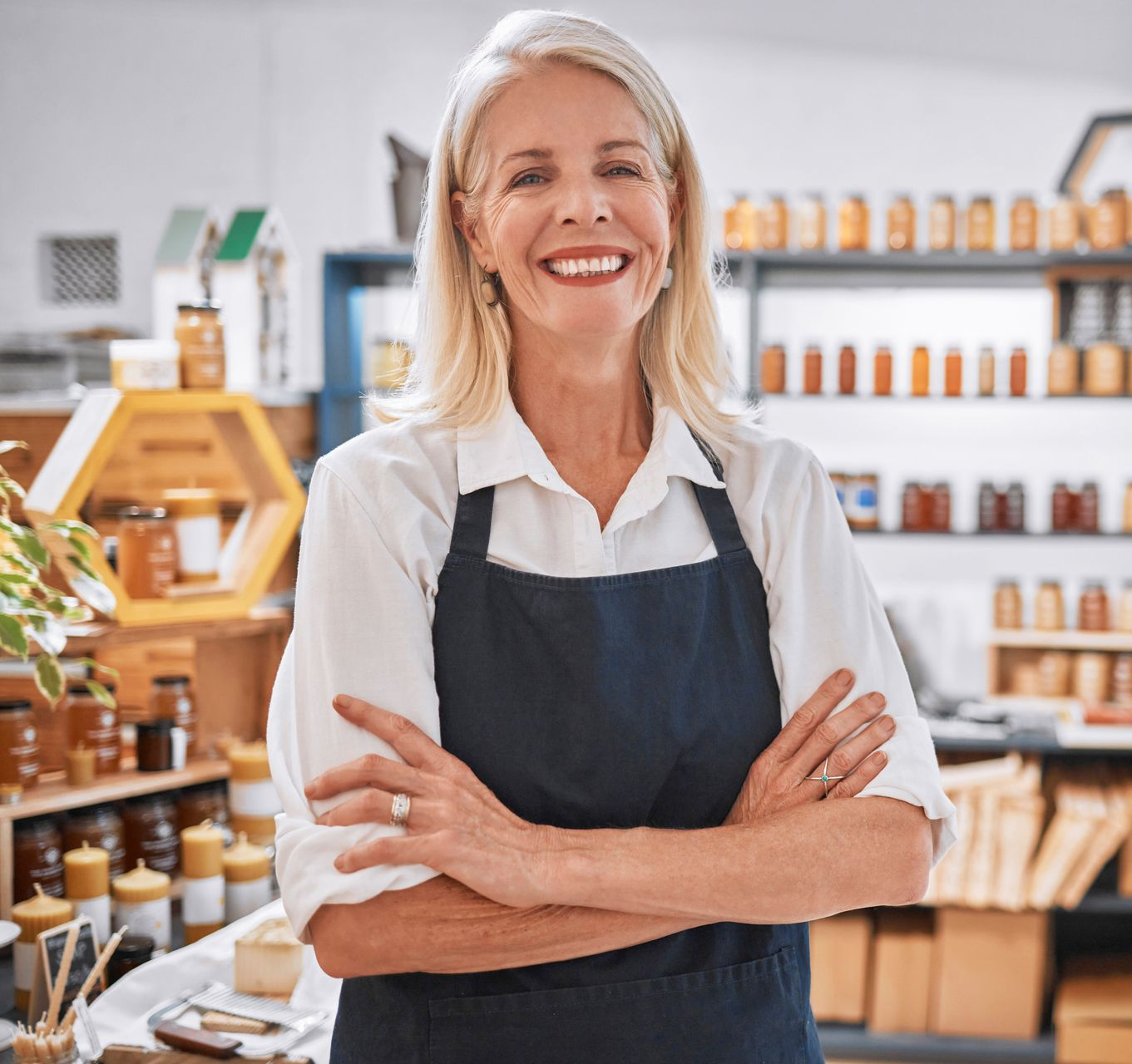 Smiling shop owner in a dark apron standing with arms crossed in a bright store