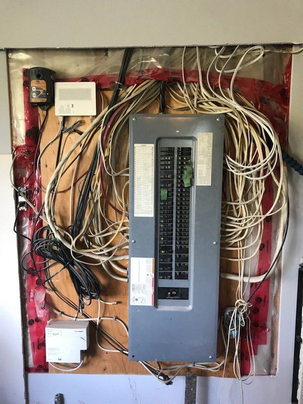 Panneau électrique avec fils emmêlés ; boîte grise avec interrupteurs sur une planche de bois.