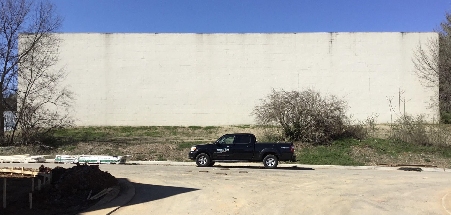 A black truck is parked in front of a large white wall.