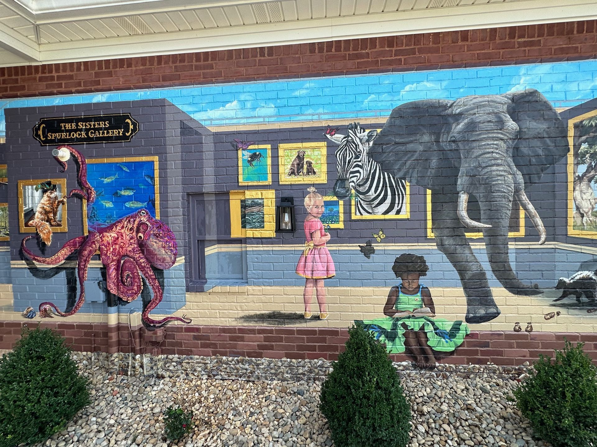 A mural of an elephant , zebra , octopus and a girl on a brick wall.