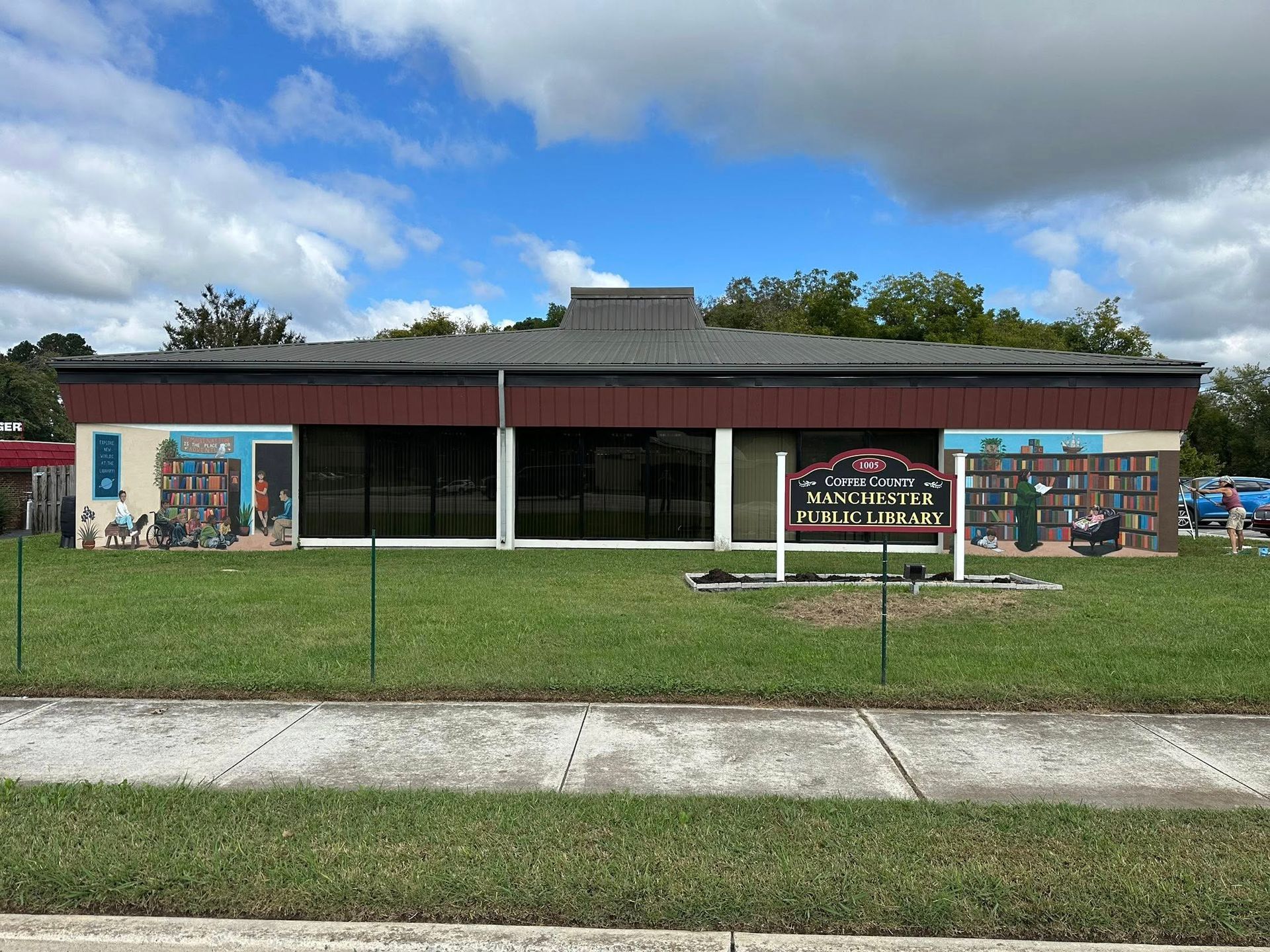 Exterior of the Wauchula Memorial Public Library with murals on the sides, grassy yard, and sign.
