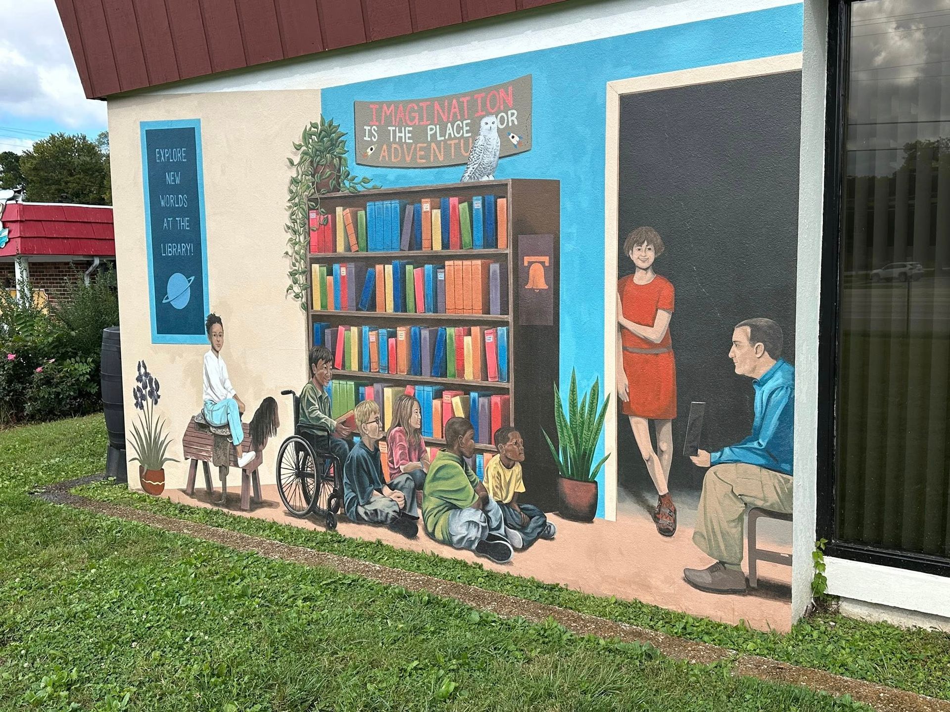 Mural: a library scene with people, bookshelves, and a door on a building exterior. Blue, orange, and tan colors.