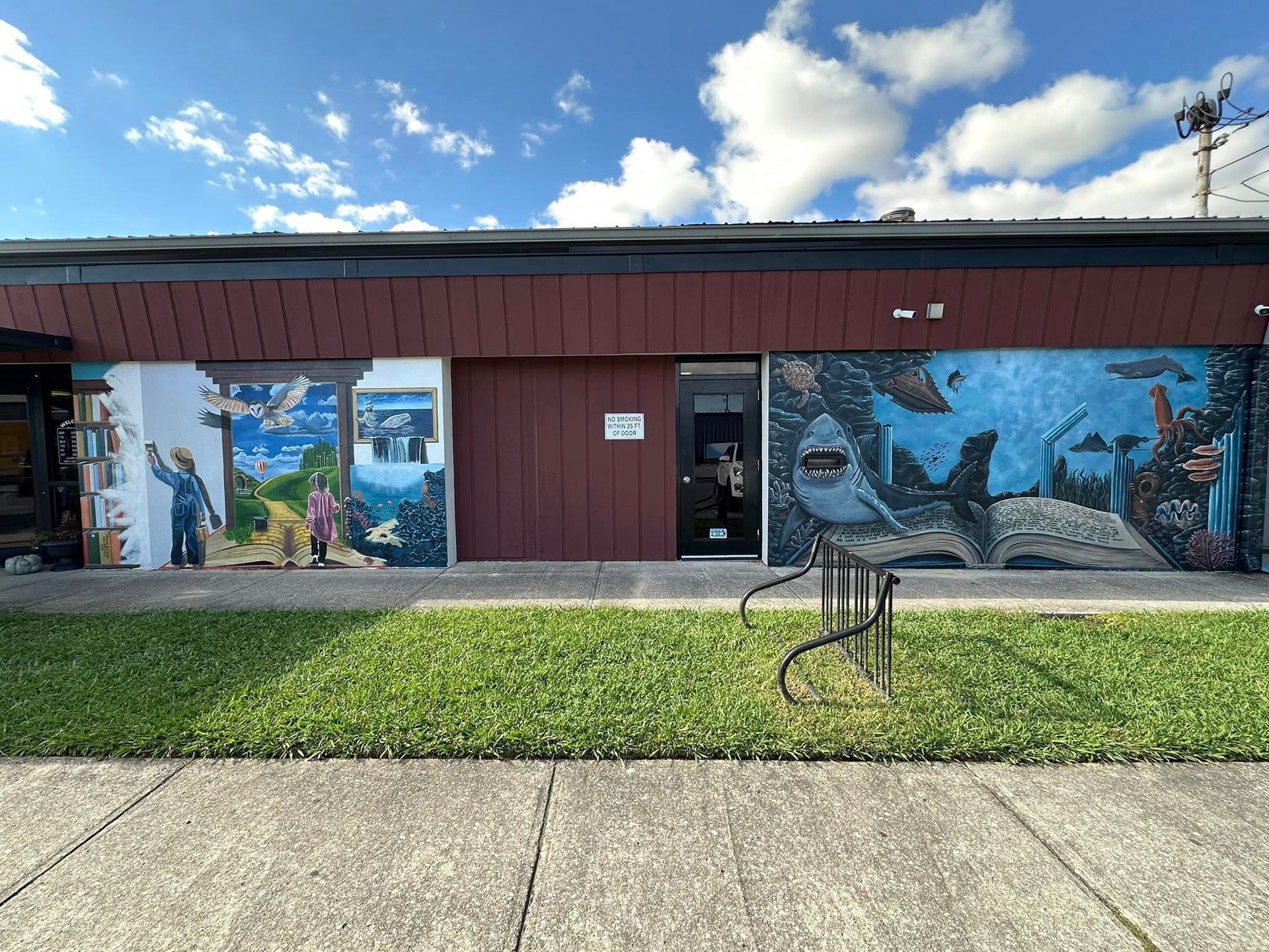 Exterior of building with murals and grass in front.