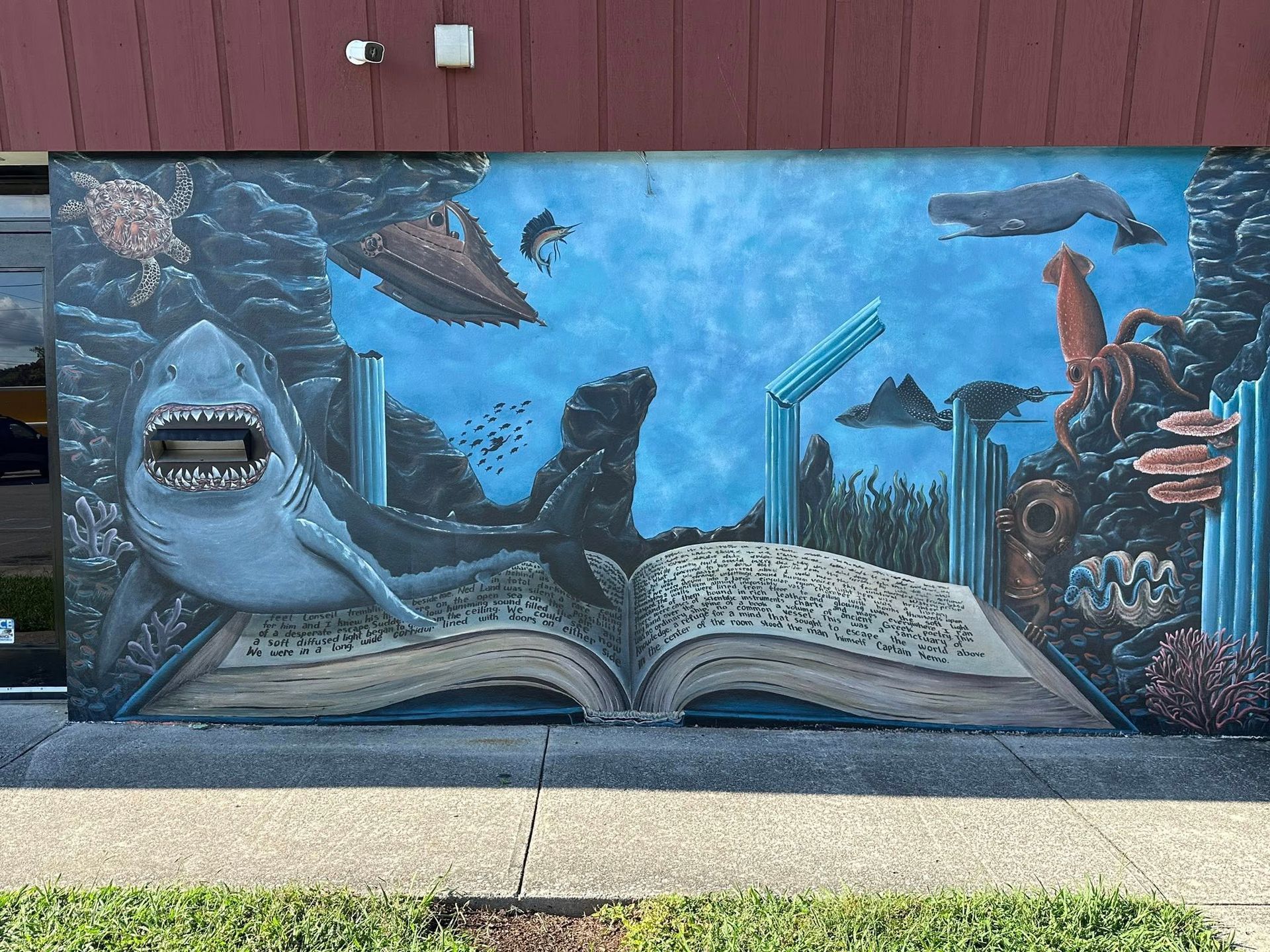 Mural of an open book with an ocean scene. Shark, whale, and squid swim around the pages, against a blue background.