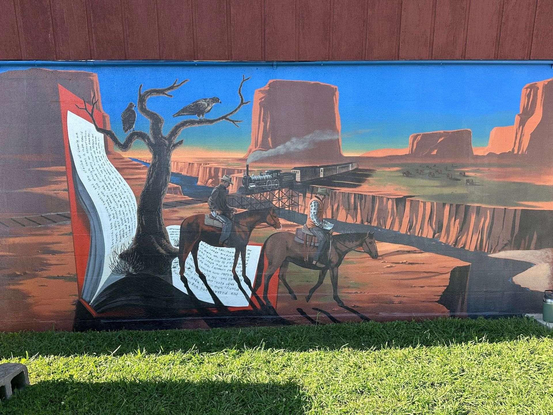 Mural of a western desert scene with two riders on horseback, a tree with birds, and a book spilling into the landscape.