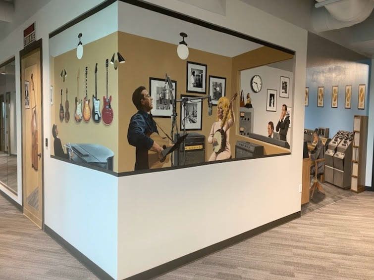 A man is playing a guitar in a room with guitars on the wall.