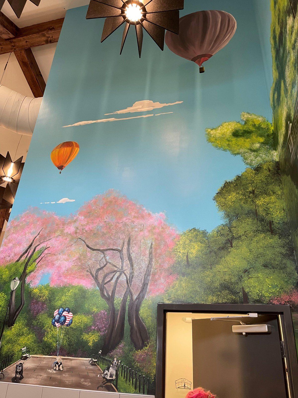 A painting of hot air balloons flying over a forest on a wall.