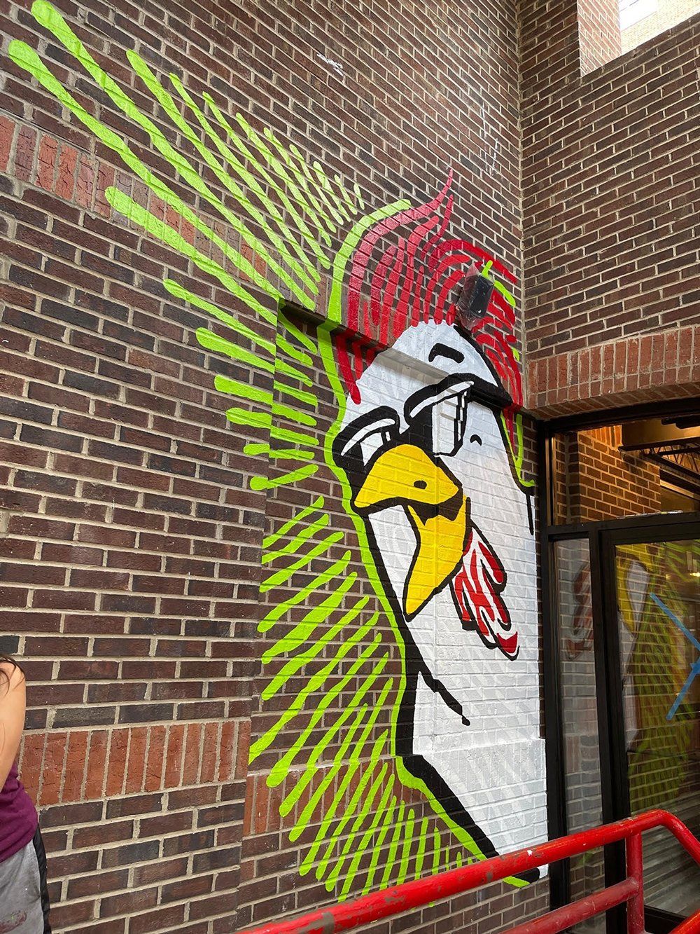 A mural of a chicken wearing sunglasses on a brick wall.