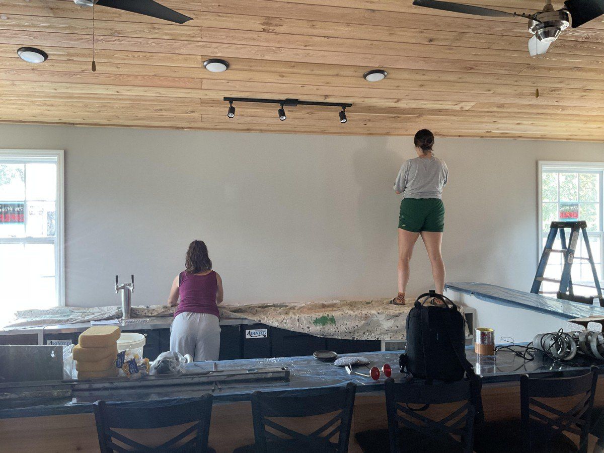 Two women are painting a wall in a kitchen.