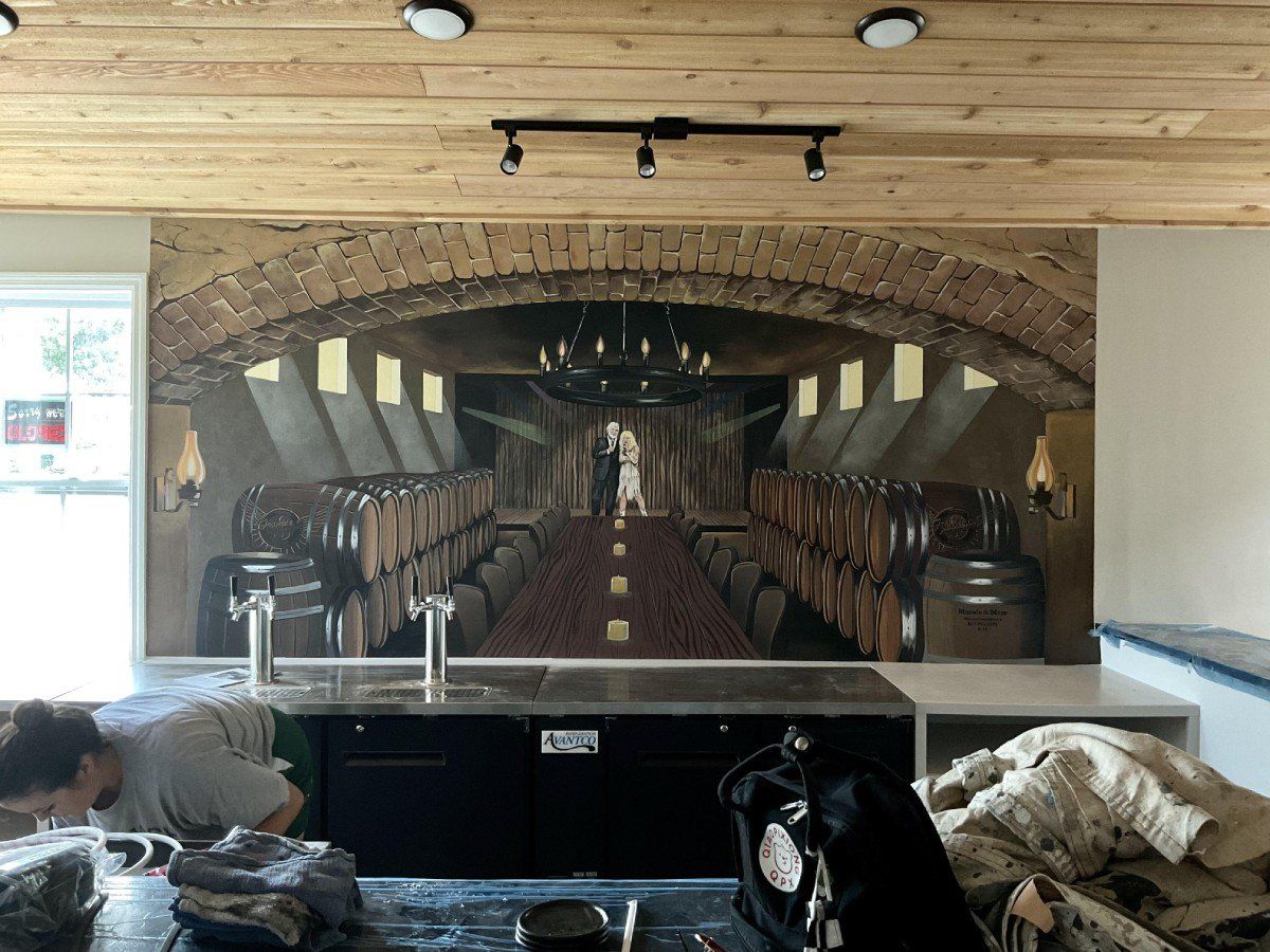 A man is working on a mural of a wine cellar in a kitchen.
