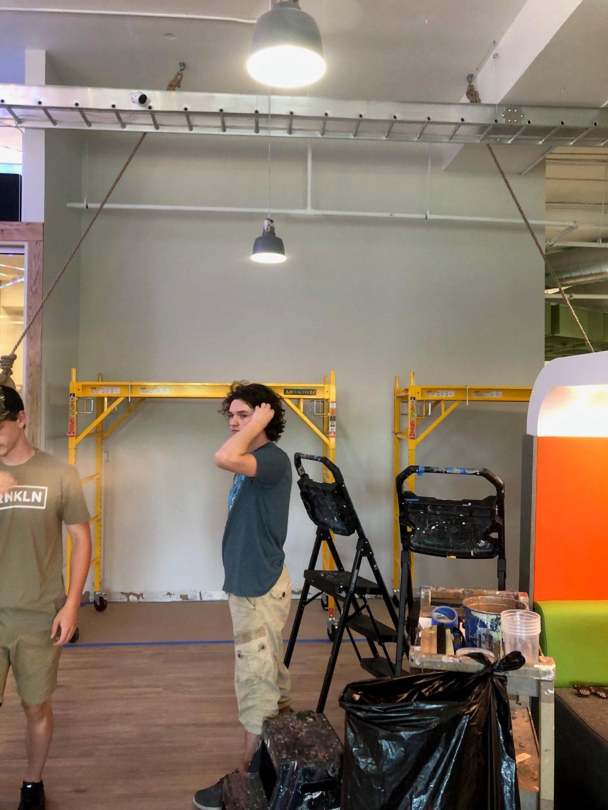 Two men are standing in a room with a chair and a ladder