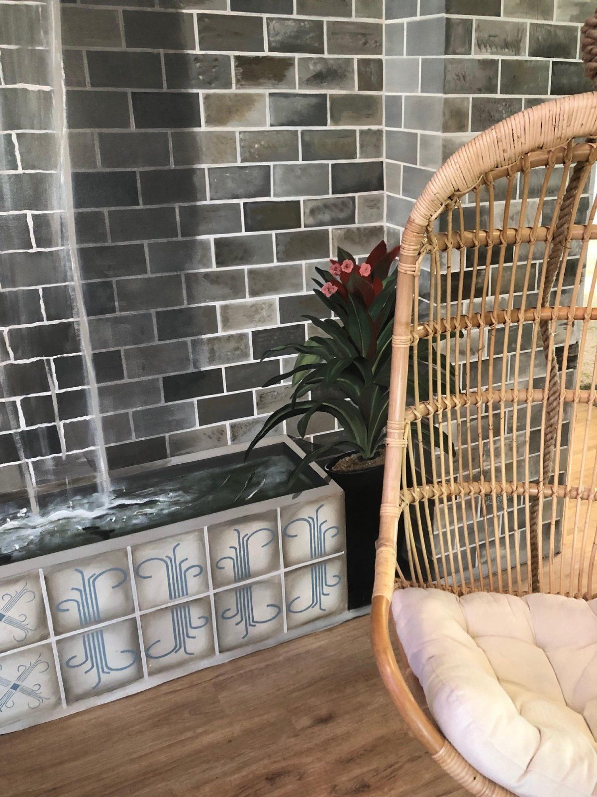 A wicker chair is sitting in front of a waterfall in a room.