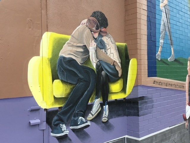 A painting of a man and woman hugging on a yellow couch