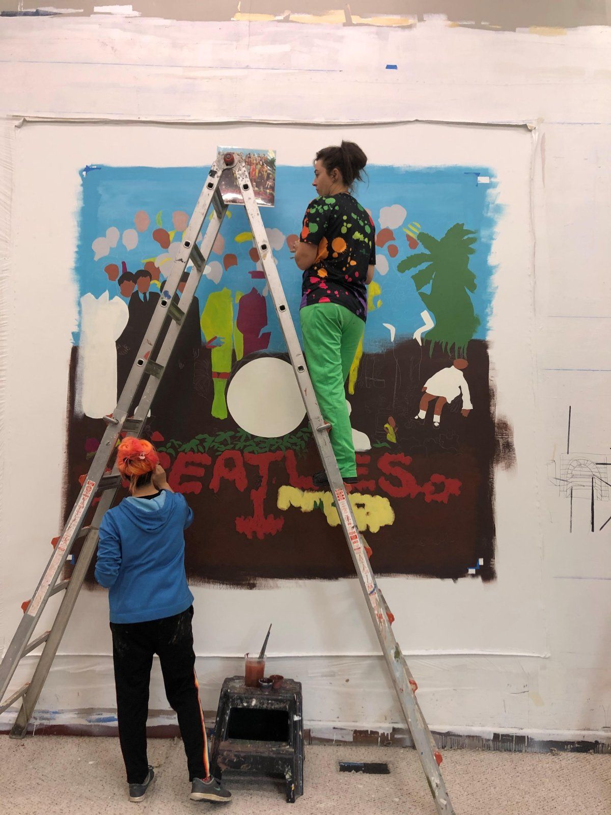 Two people are painting a mural of the beatles on a wall