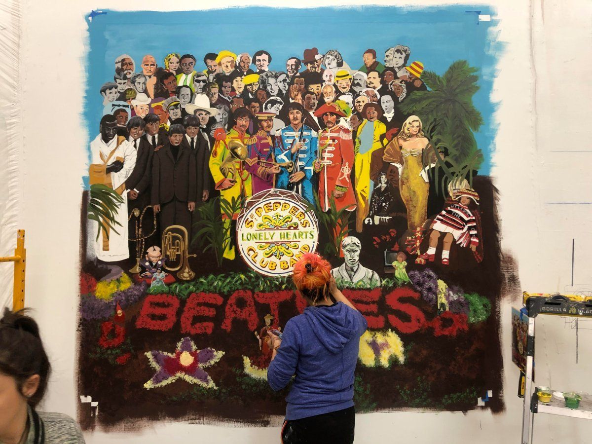 A woman is painting a mural of the beatles on a wall