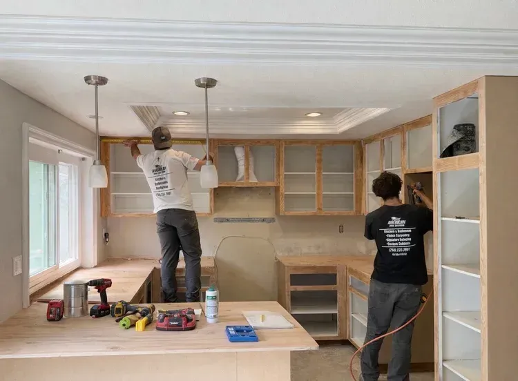 Two people installing kitchen cabinets in a bright room with a countertop and tools.