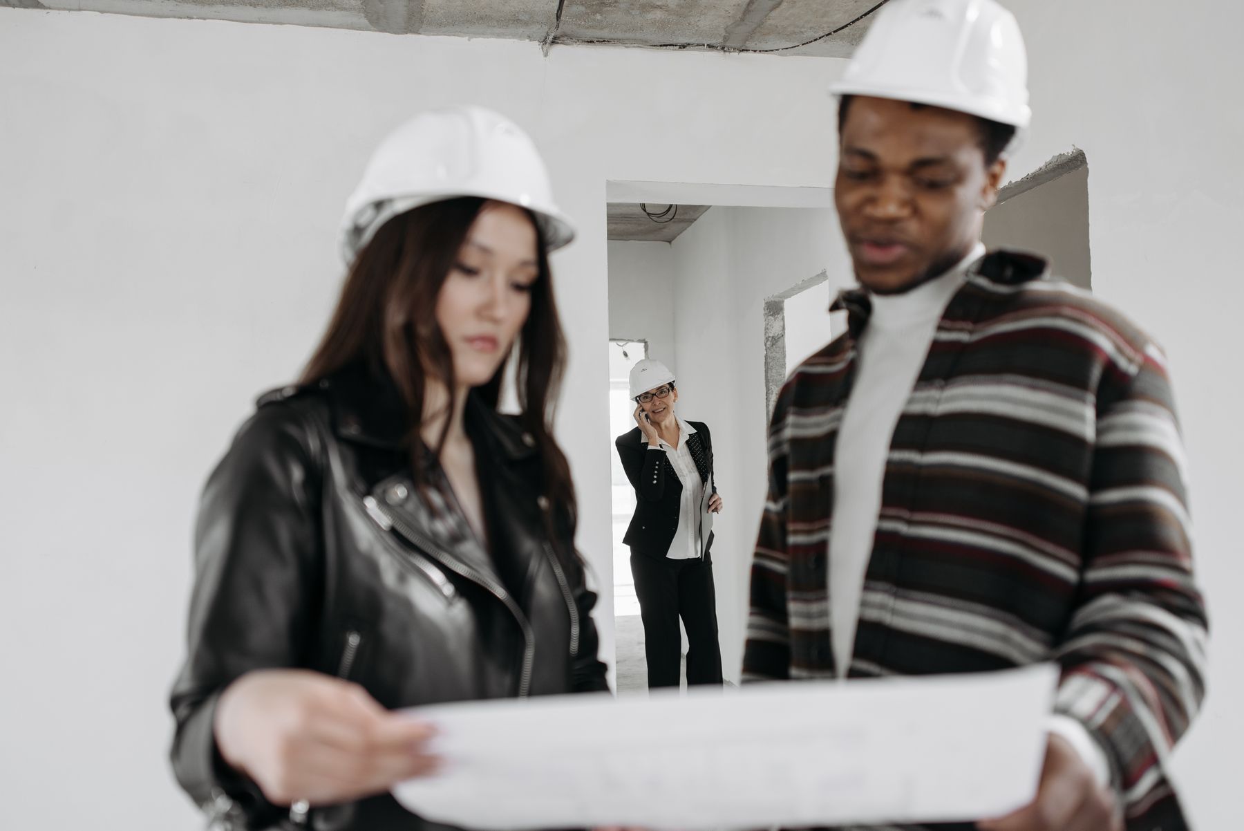 Two workers in hard hats reviewing a blueprint indoors