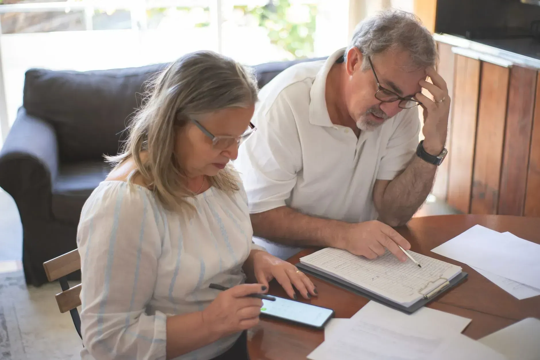 Two people review documents at a table, one using a phone and the other writing in a notebook.