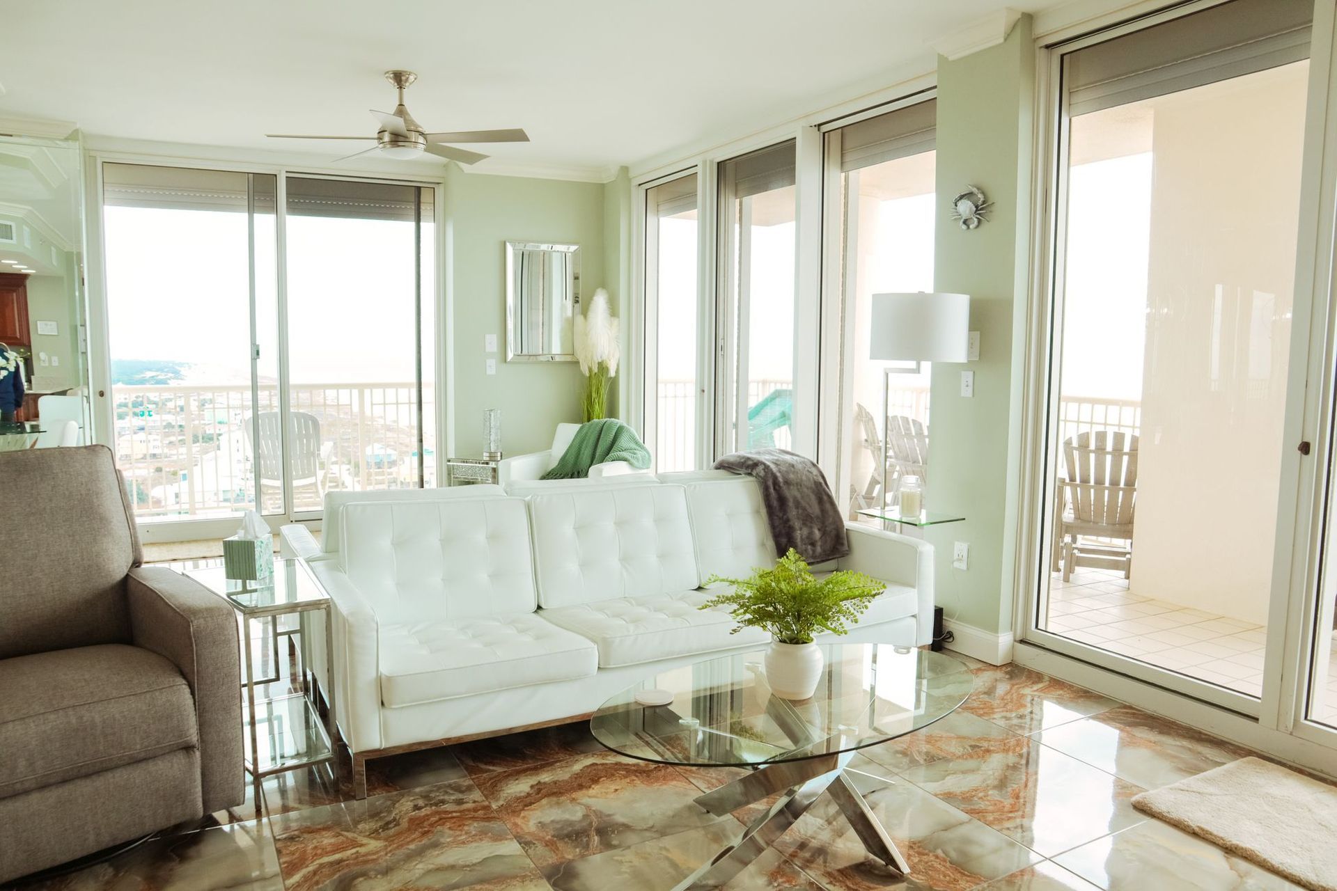 Bright living room with white sofa, glass coffee table, and balcony doors with sunlight.
