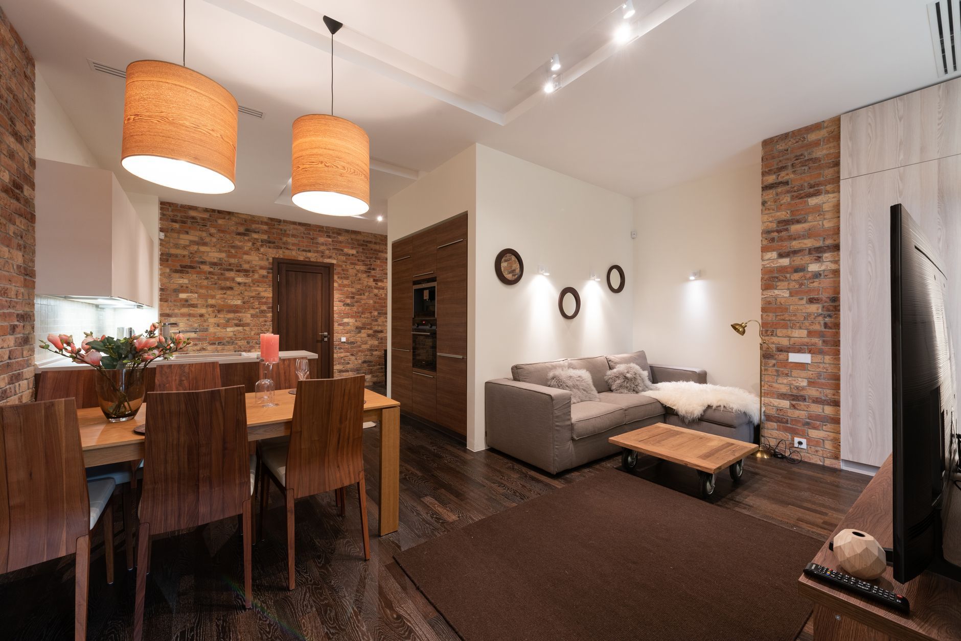 Modern open-plan living room with sofa, dining table, brick accents, and a wall-mounted TV