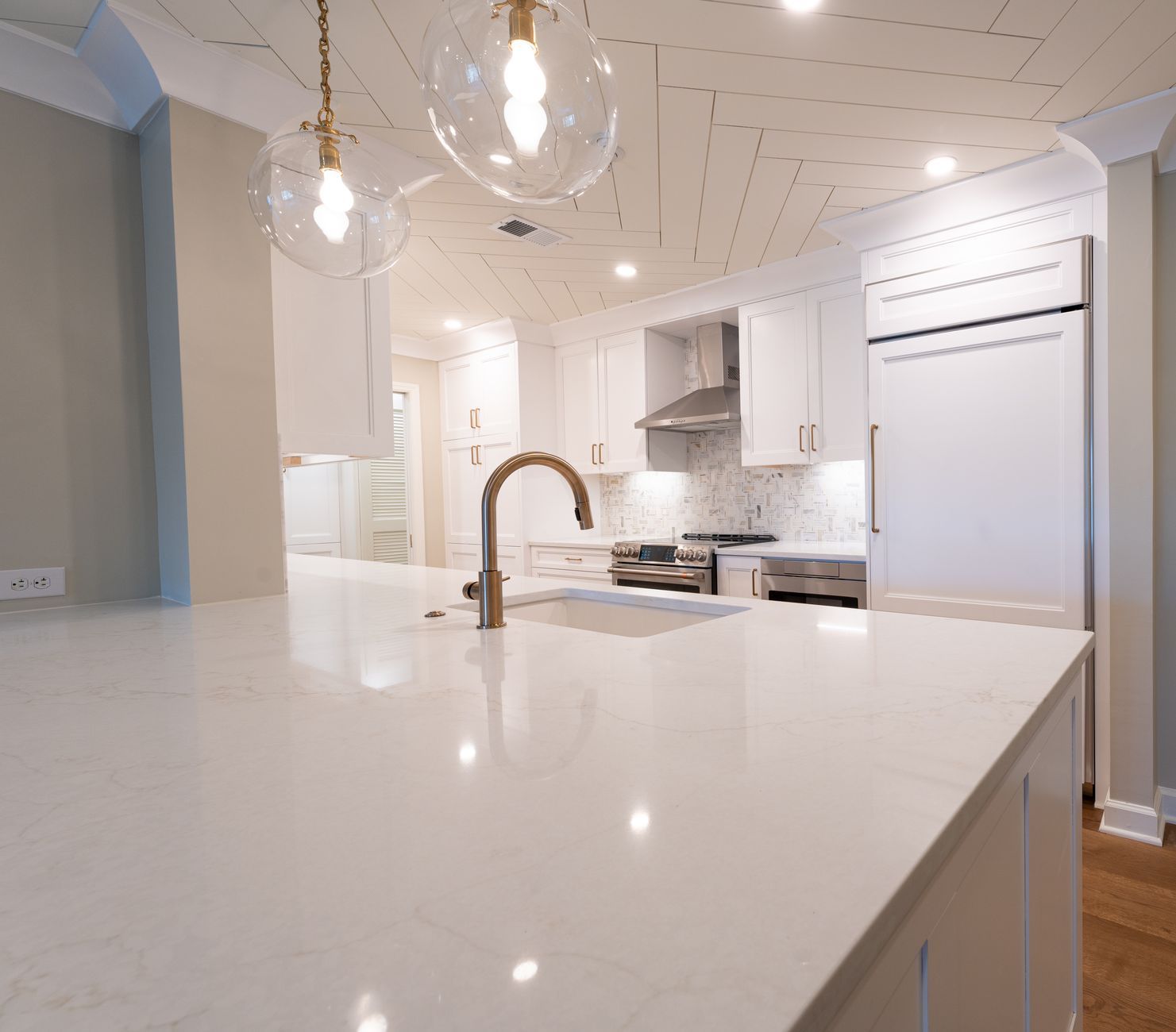 Bright modern kitchen with white island, gold faucet, pendant lights, and stainless steel appliances