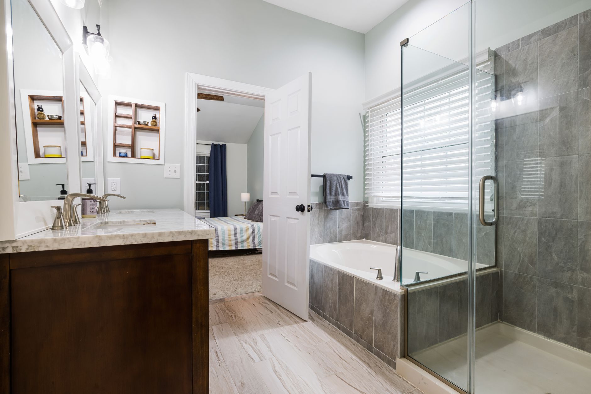 Bright modern bathroom with double vanity, glass shower, and large soaking tub beside a window