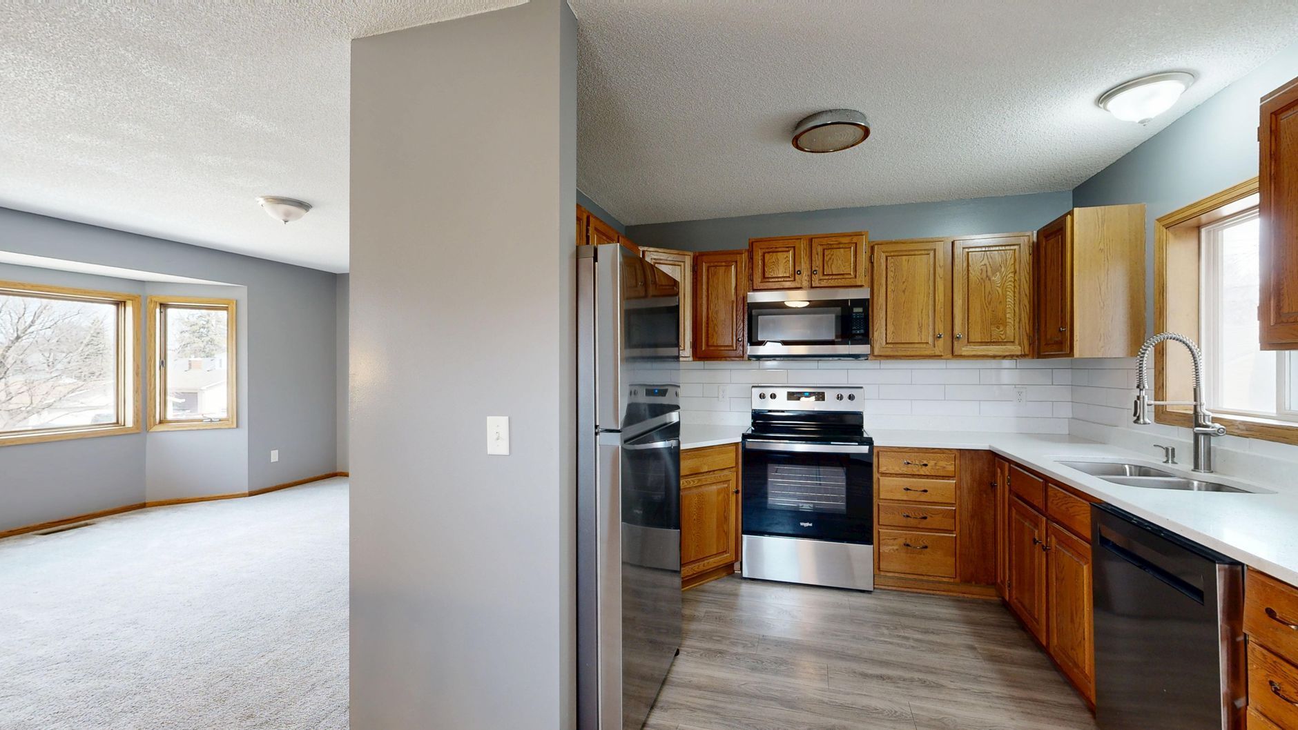 Open kitchen and adjoining living room with wood cabinets, white appliances, gray flooring, and large windows