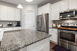 Bright modern kitchen with white cabinets, granite island, and stainless steel appliances