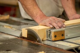 Person guiding a wooden board through a table saw in a workshop