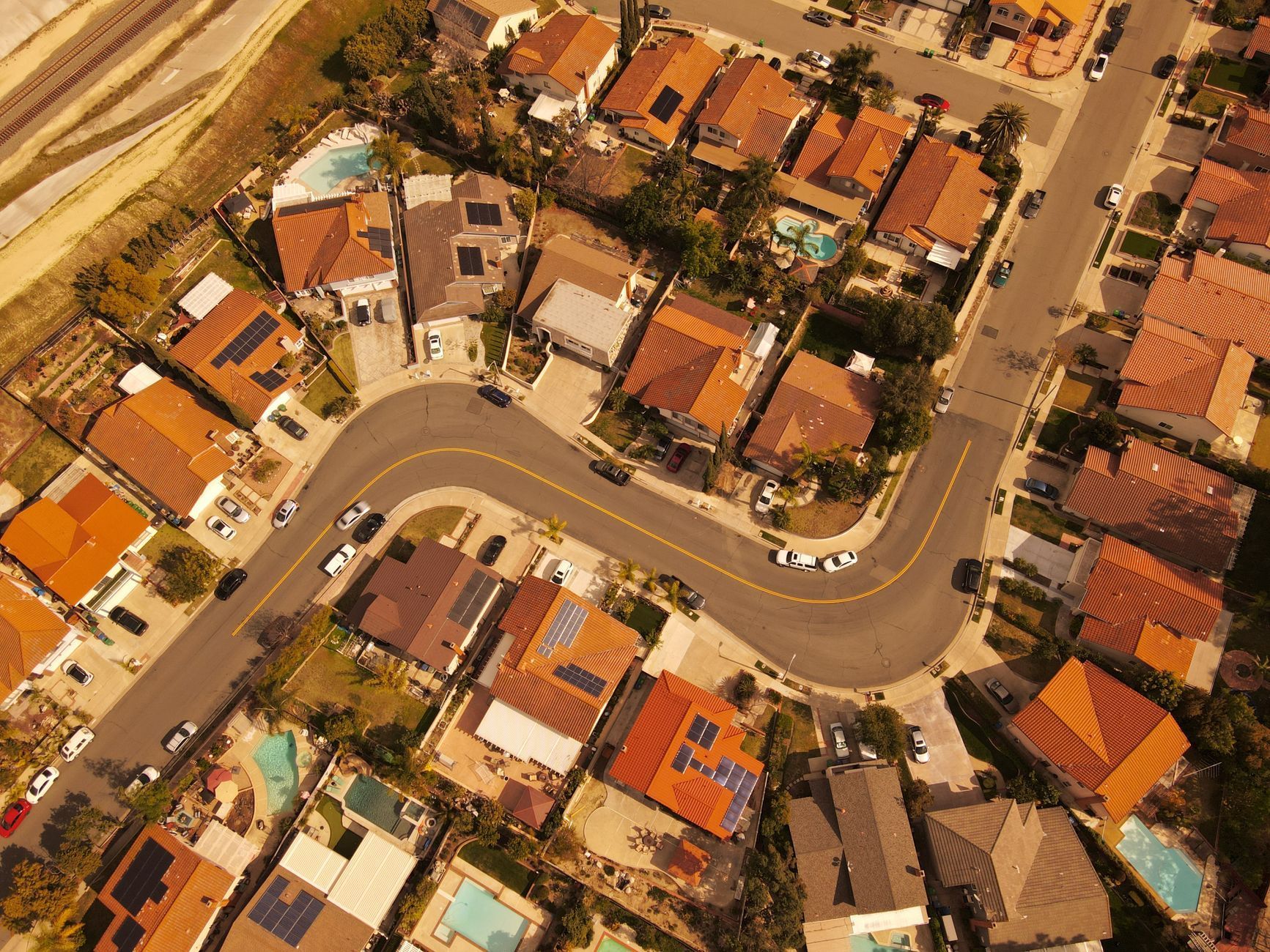 Aerial view of a curving residential street with houses, parked cars, and a swimming pool.