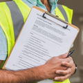 Worker in a neon safety vest holding a clipboard and pen during a site inspection