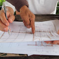 Hands marking measurements on architectural blueprints with a pencil and finger at a table
