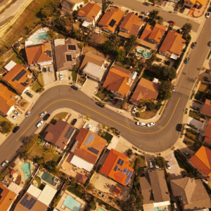 Aerial view of a curving suburban street with closely packed houses and parked cars.